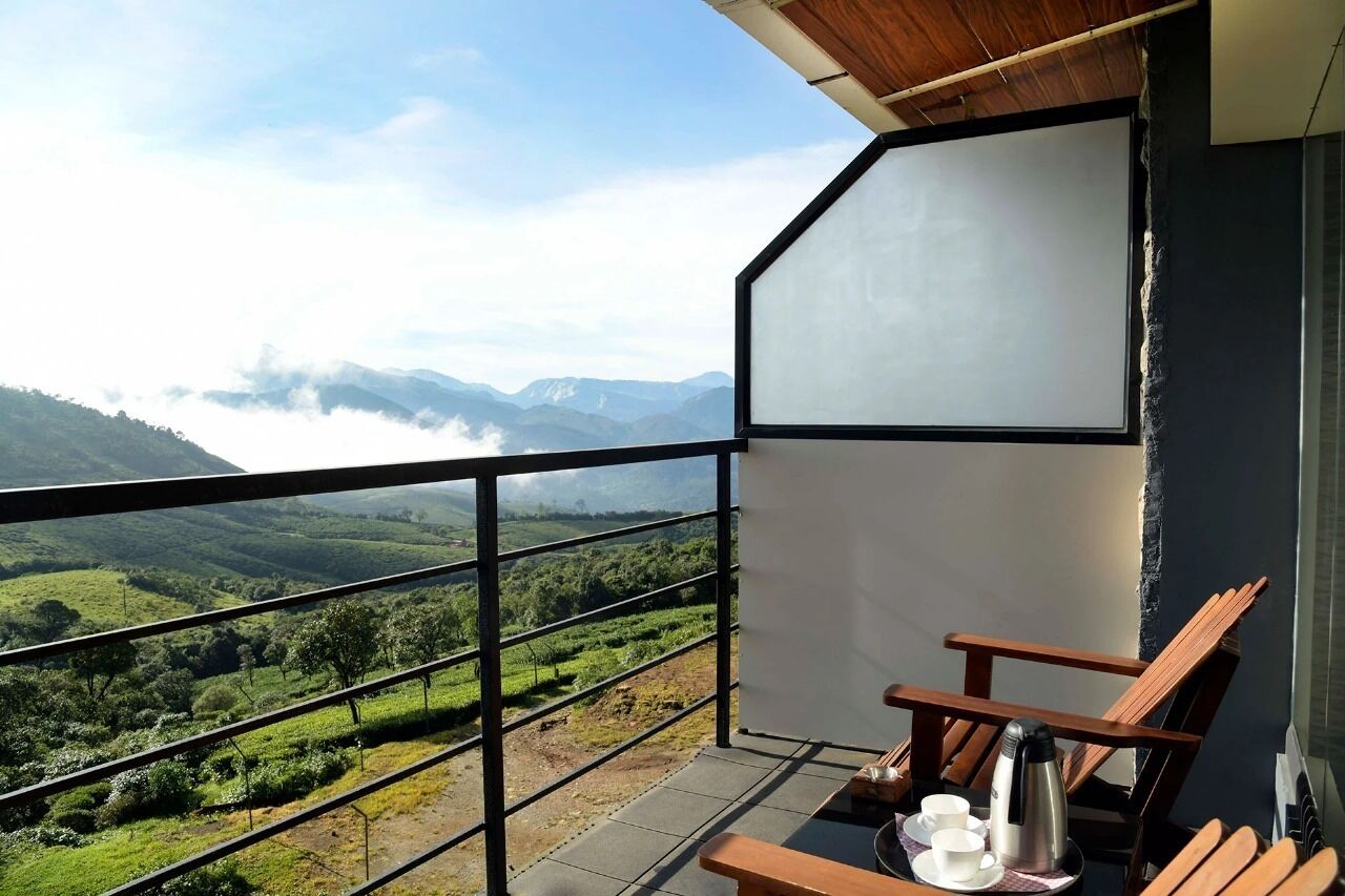 Ein Balkon mit Blick auf grüne Hügel und Berge, ein Holzsessel und ein Tisch mit Teekanne und Tassen.