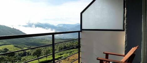 Ein Balkon mit Blick auf grüne Hügel und Berge, ein Holzsessel und ein Tisch mit Teekanne und Tassen.