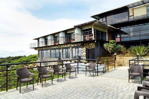 A modern building with a balcony area featuring wicker chairs and a stone wall. - Ibex Resorts, Valparai (Tale Rock) (Valparai)