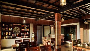A dining area with wooden furniture, a bookshelf with books, and a clock on the wall. - Ibex Resorts, Valparai (Tale Rock) (Valparai)
