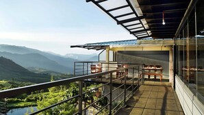A balcony with a view of a mountainous landscape, a covered outdoor seating area, and a modern architectural design. - Ibex Resorts, Valparai (Tale Rock) (Valparai)
