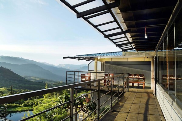 A balcony with a view of a mountainous landscape, a covered outdoor seating area, and a modern architectural design. - Ibex Resorts, Valparai (Tale Rock) (Valparai)