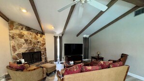 A living room with a stone fireplace, a sofa set, a television, and a ceiling fan. - CHARMING! 3-bedroom house with Pool, WiFi, AC in marvelous Fort Myers near beach (Fort Myers)