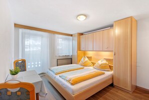 Une chambre à coucher avec un lit, une armoire en bois, une table avec une plante et une chaise.