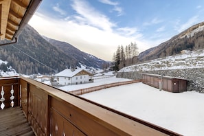 Un balcon en bois surplombant un paysage montagneux enneigé, avec un mur de pierre et un bâtiment en bois.
