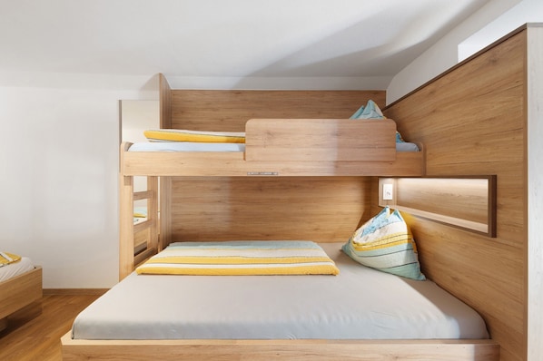 A bunk bed with a wooden headboard, a lower bed with a pillow, and a bedside table.