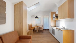 A modern kitchen with wooden cabinets, a dining area with a bench, and a sofa. - Studio 'Waldheim Apt 4' with Mountain View, Shared Garden and Wi-Fi (Ahrntal)