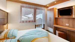 Ein Schlafzimmer mit einem Bett, einem an der Wand montierten Fernseher und einem Fenster mit Blick auf eine verschneite Landschaft.