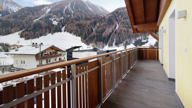 Ein Balkon mit Holzbalkon, der auf eine gebirgige Landschaft blickt.