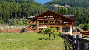 Ein mehrstöckiges Gebäude mit Balkon, beschriftet mit 'Pension Waldheim', umgeben von einer grünen Wiese und bewaldeten Hügeln.