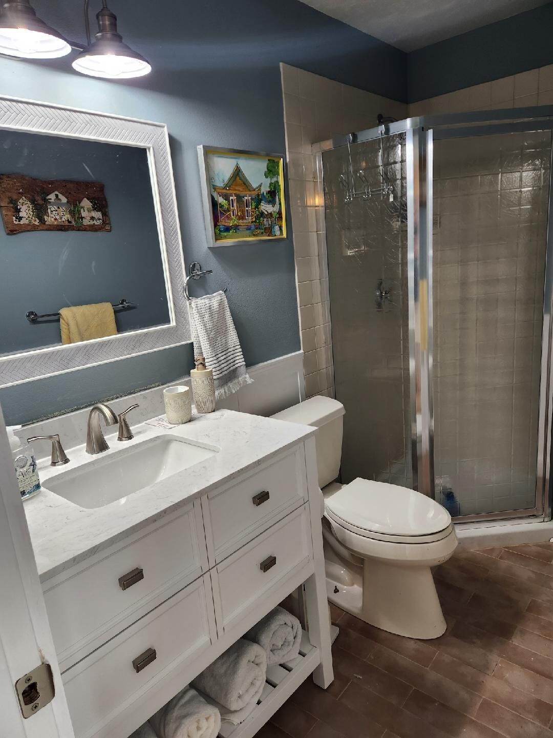 Un baño con tocador doble lavamanos, inodoro, cabina de ducha con mampara de vidrio y un espejo grande.