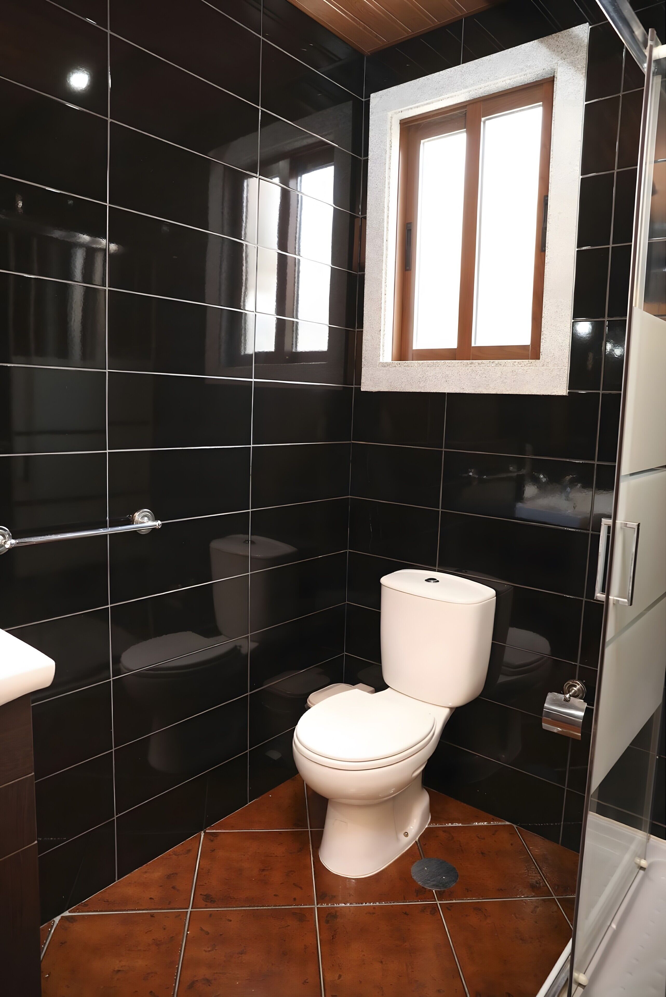 A bathroom with black tiled walls, a white toilet, and a window above the sink.