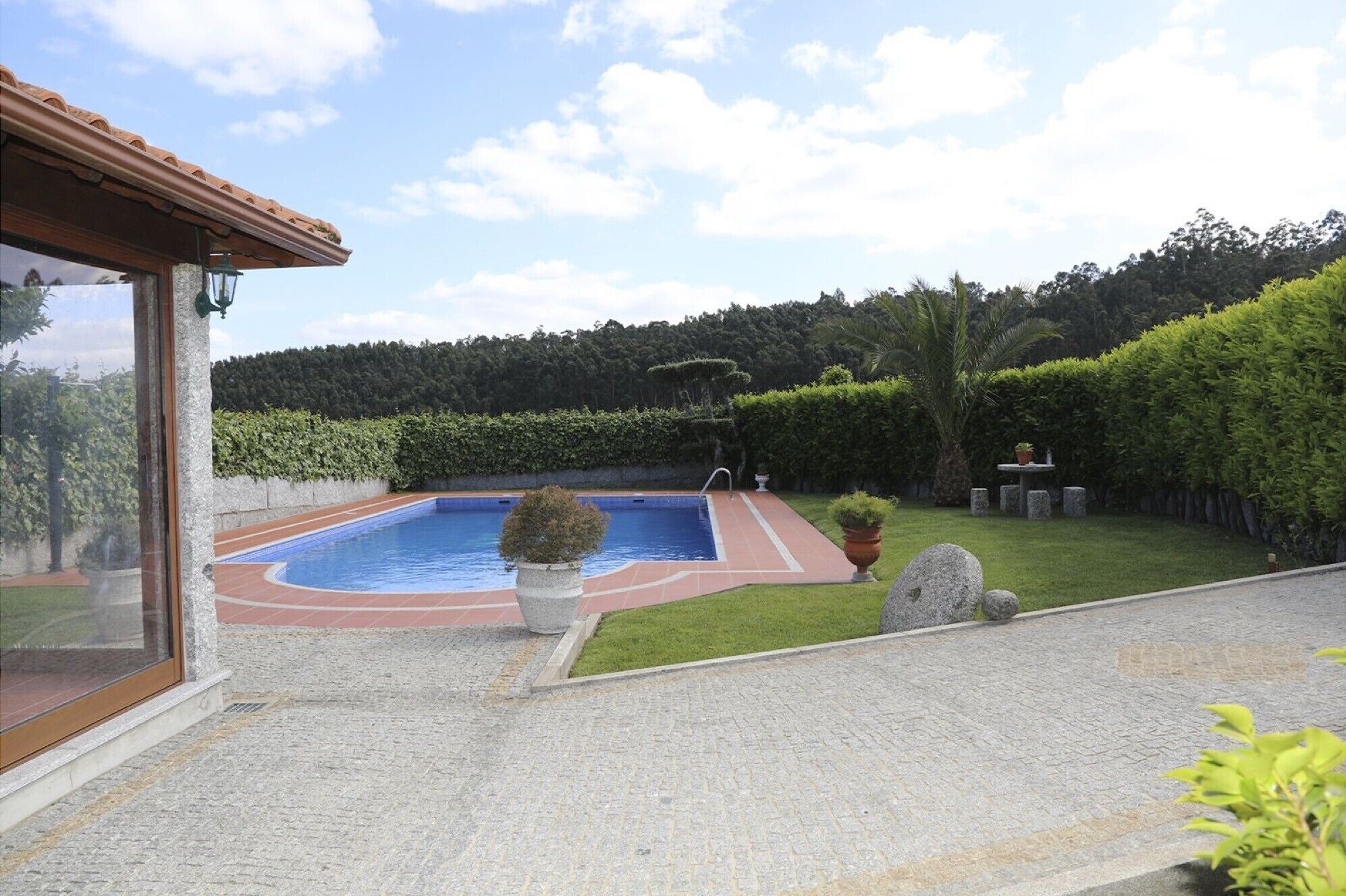 A swimming pool with a tiled deck, surrounded by a well-maintained lawn and hedges.