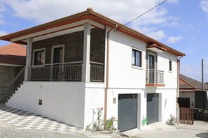 Un edificio de dos pisos con un balcón, un garaje y un pavimento a cuadros al frente.
