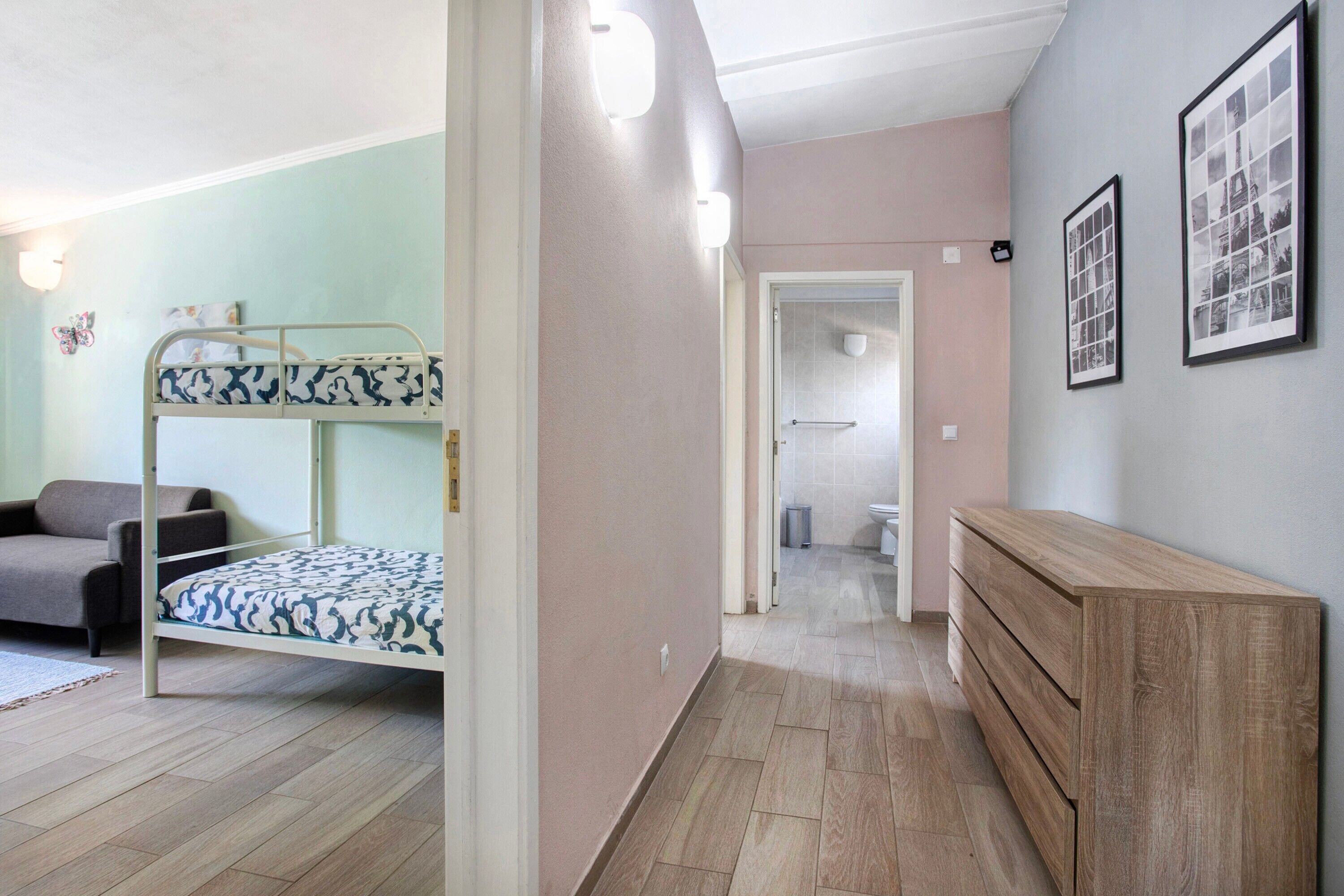Een kamer met een stapelbed, een slaapbank, een houten dressoir en een gang naar een badkamer.