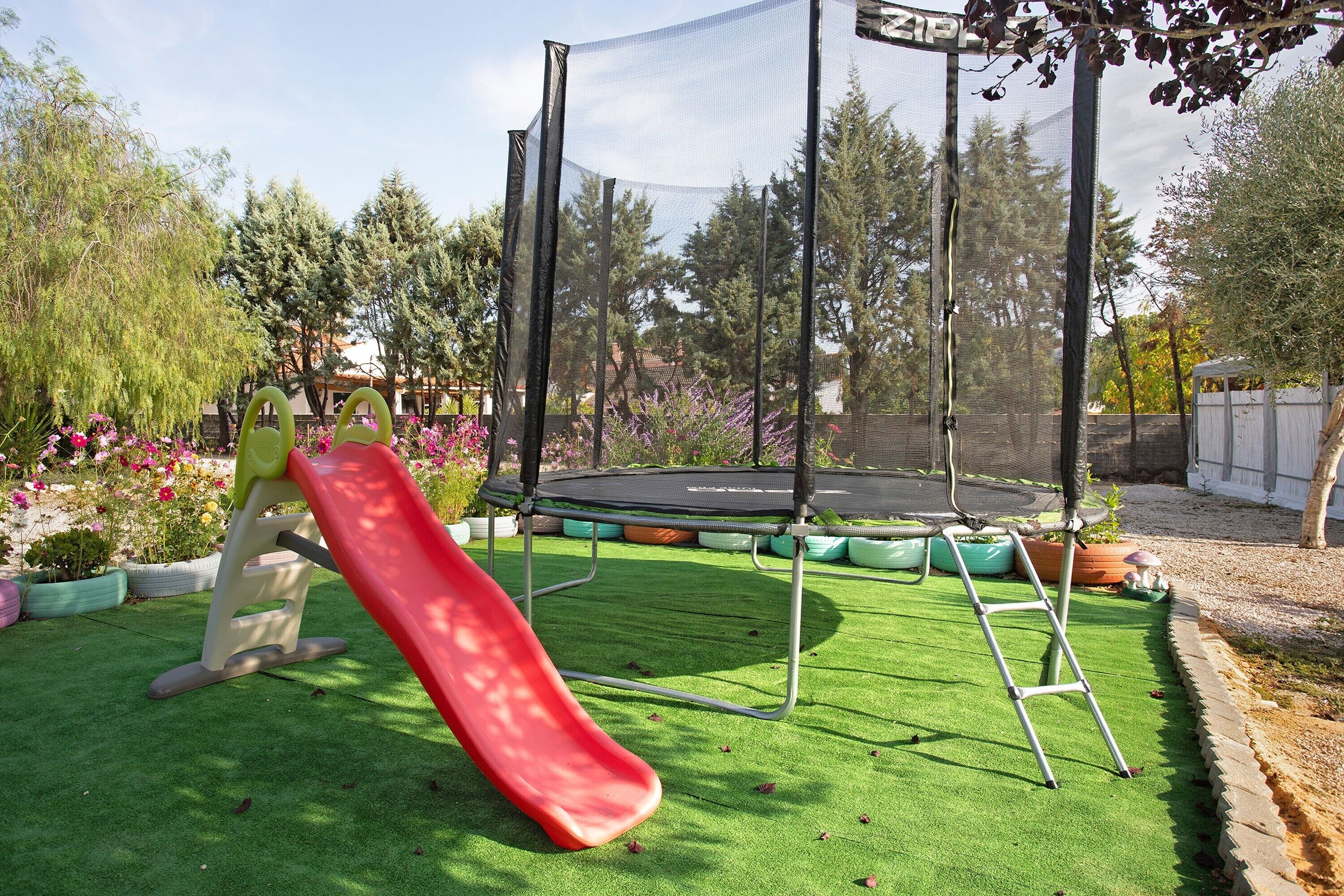 Ein Garten mit Trampolin, Rutsche und künstlichem Rasen.