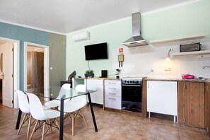 A modern kitchen with a glass dining table, white cabinets, a stove, and a TV mounted on the wall. - Holiday Home 'Casa 2' with Shared Pool, Wi-Fi and Air Conditioning (Vale da Pedra)
