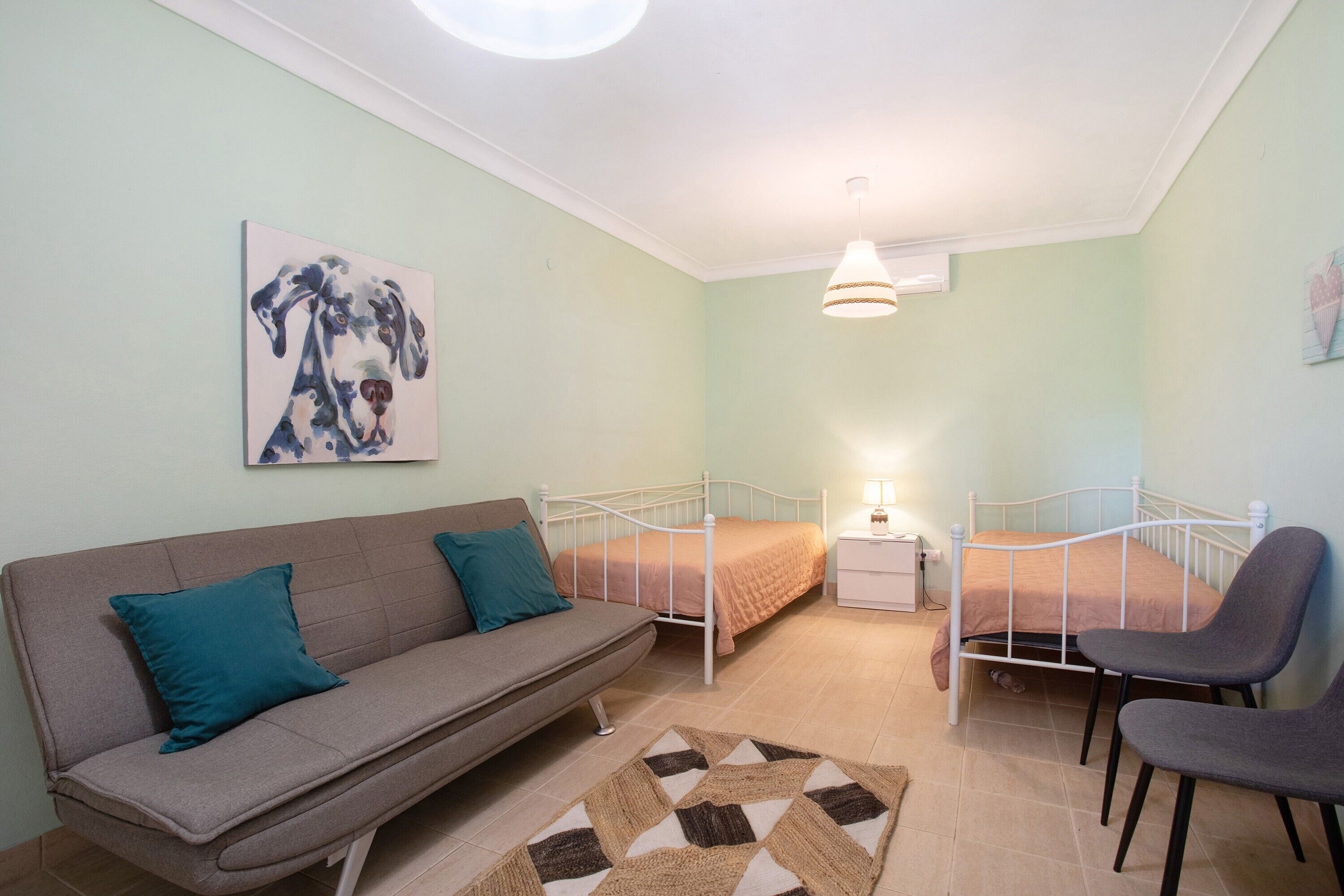 Ein Schlafzimmer mit einer Schlafcouch, einem Bett, einem Sessel, einem Nachttisch und einer Wandlampe.