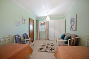 Une pièce avec deux lits, un canapé, une chaise, une fenêtre avec des rideaux et une porte.
