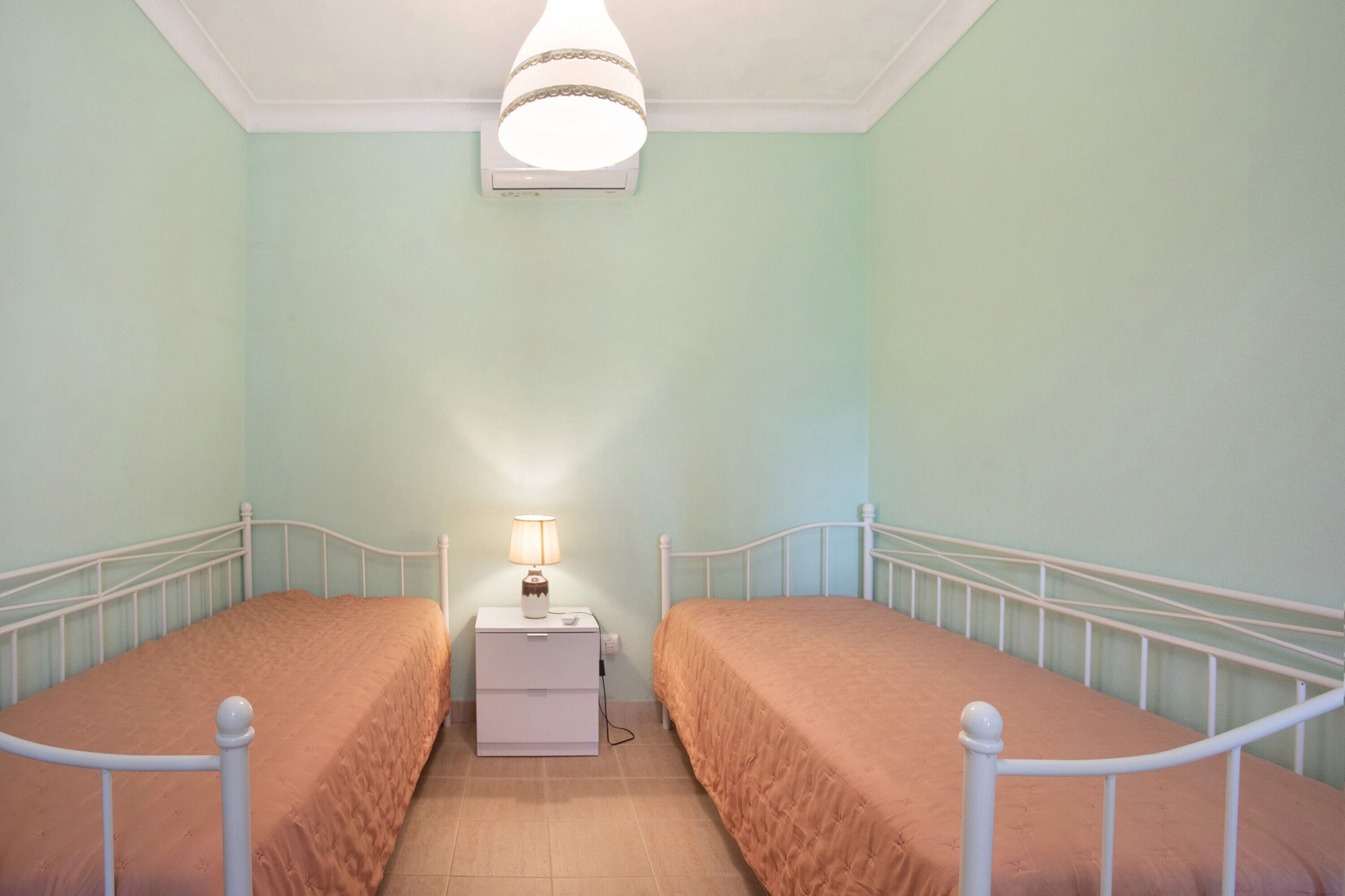 A twin room with two single beds, a bedside table with a lamp, and a ceiling fan.