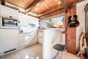 Una cocina con armarios blancos, un horno Bosch, techo de madera, una ventana y una guitarra.