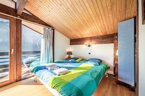 A bedroom with a bed, a window, a door, and a wall-mounted light fixture.