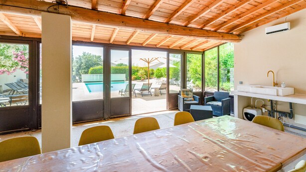 Un espace extérieur abrité, aménagé pour les repas, avec une table et des chaises, une piscine et une vue sur la verdure.