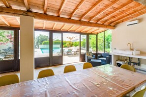 Un espace extérieur abrité, aménagé pour les repas, avec une table et des chaises, une piscine et une vue sur la verdure.