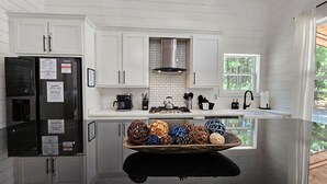 Una cocina moderna con armarios blancos, una campana extractora de acero inoxidable, una cafetera y un estante de madera con adornos.