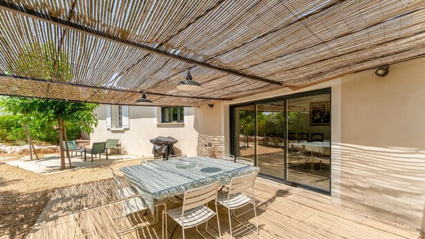 An outdoor patio with a table and chairs, a pergola, and a glass door leading to an interior space. - Holiday Home 'Saumane, Grande Bergerie' with Shared Pool, Wi-Fi and Air Conditioning (Saumane-de-Vaucluse)