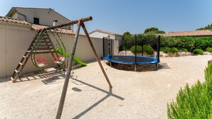 A backyard with a swing set, trampoline, and a ladder leaning against a wall. - Holiday Home 'Saumane, Grande Bergerie' with Shared Pool, Wi-Fi and Air Conditioning (Saumane-de-Vaucluse)