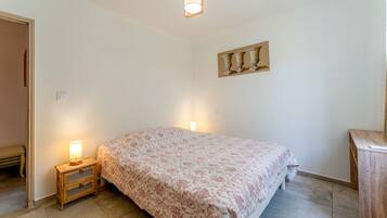 A bedroom with a bed, bedside lamps, a wooden nightstand, a wall-mounted picture, and a door.