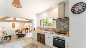 A modern kitchen with a dining area, a clock, and a window. - Holiday Home 'Saumane, Grande Bergerie' with Shared Pool, Wi-Fi and Air Conditioning (Saumane-de-Vaucluse)