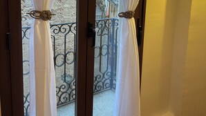 A room with a balcony featuring white curtains with decorative ties, a metal railing, and a view of a building with a red dome. - Ulls del Priorat (El Masroig)