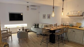 A modern kitchen with a dining area, wooden flooring, and a flat-screen TV mounted on the wall. - Ulls del Priorat (El Masroig)