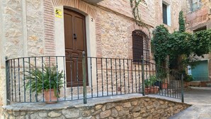 A stone building with a metal railing, a brown door, and potted plants. - Ulls del Priorat (El Masroig)