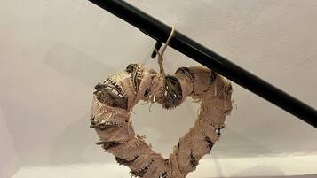 A heart-shaped decoration made of burlap and twine, hanging from a black rod against a white wall.