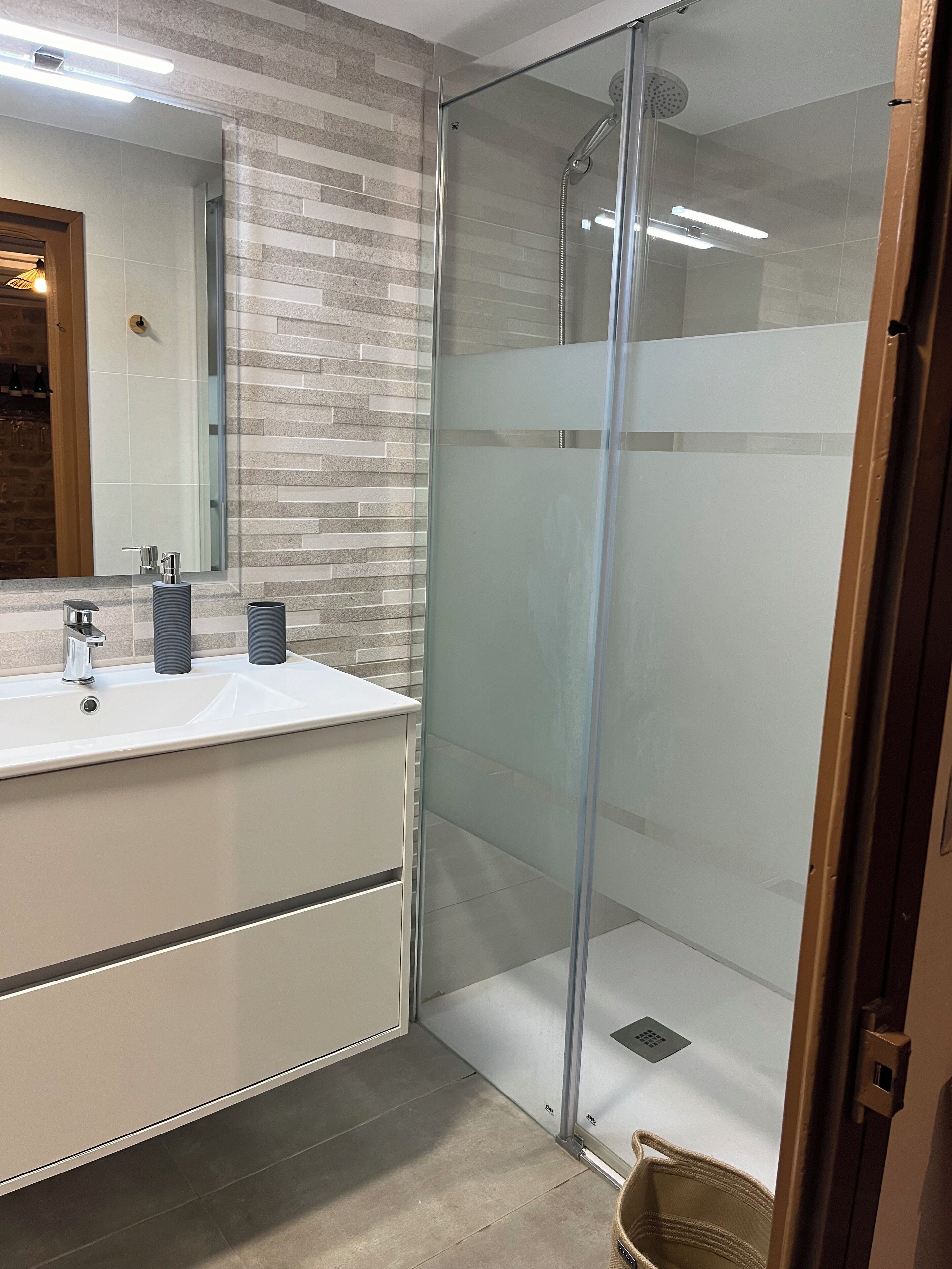 Een moderne badkamer met een douche met glazen wand, een wit wastafelmeubel met twee wasbakken en een spiegel erboven.