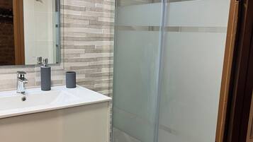 Een moderne badkamer met een douche met glazen wand, een wit wastafelmeubel met twee wasbakken en een spiegel erboven.