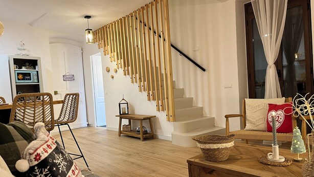 A cozy living room with a wooden staircase, a dining area with wicker chairs, and a kitchen with a blue appliance. - Ulls del Priorat (El Masroig)