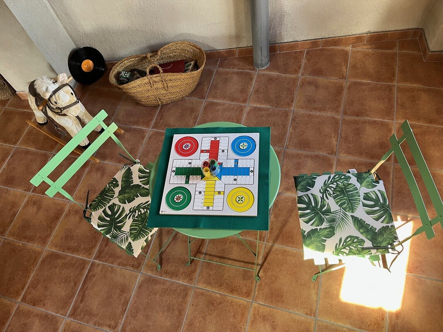 Ein kleiner Tisch mit einem Brettspiel, einem Spielpferd, einem Korb voller Gegenstände und einer Pflanze.