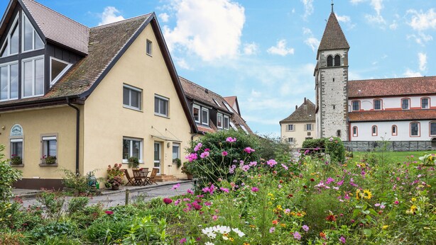 A traditional European-style building with a prominent tower, surrounded by a well-maintained garden with various flowers. - Apartment 2 in Haus Böhler on the island of Reichenau with Lake View, Terrace and Garden (Reichenau)
