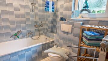 Ein Badezimmer mit Badewanne, Toilette, Dusche und einem Fenster mit Blick ins Freie.