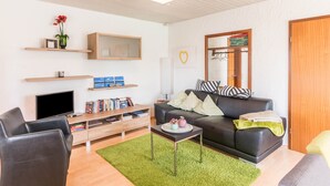 Un salon moderne avec un téléviseur à écran plat, un canapé, une table basse et une bibliothèque.