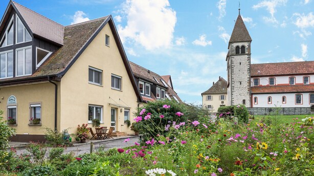 Une maison européenne traditionnelle dotée d’une tour, entourée d’un jardin où poussent différentes sortes de fleurs.