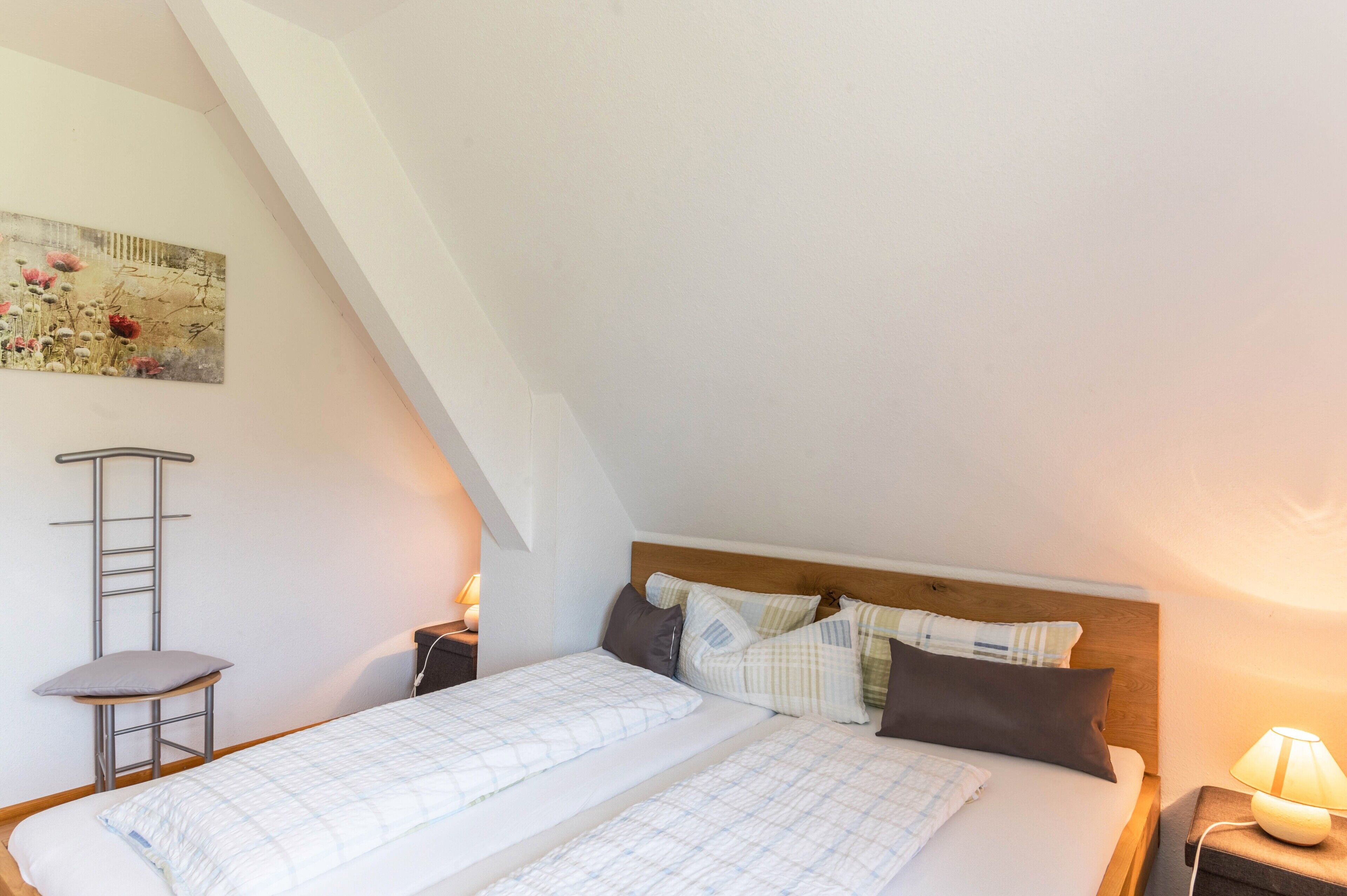 A bedroom with a loft bed, a ladder, a bedside table with a lamp, and a painting on the wall.