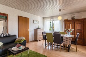 A modern living room with a sofa, dining table, chairs, and a kitchen area with cabinets.