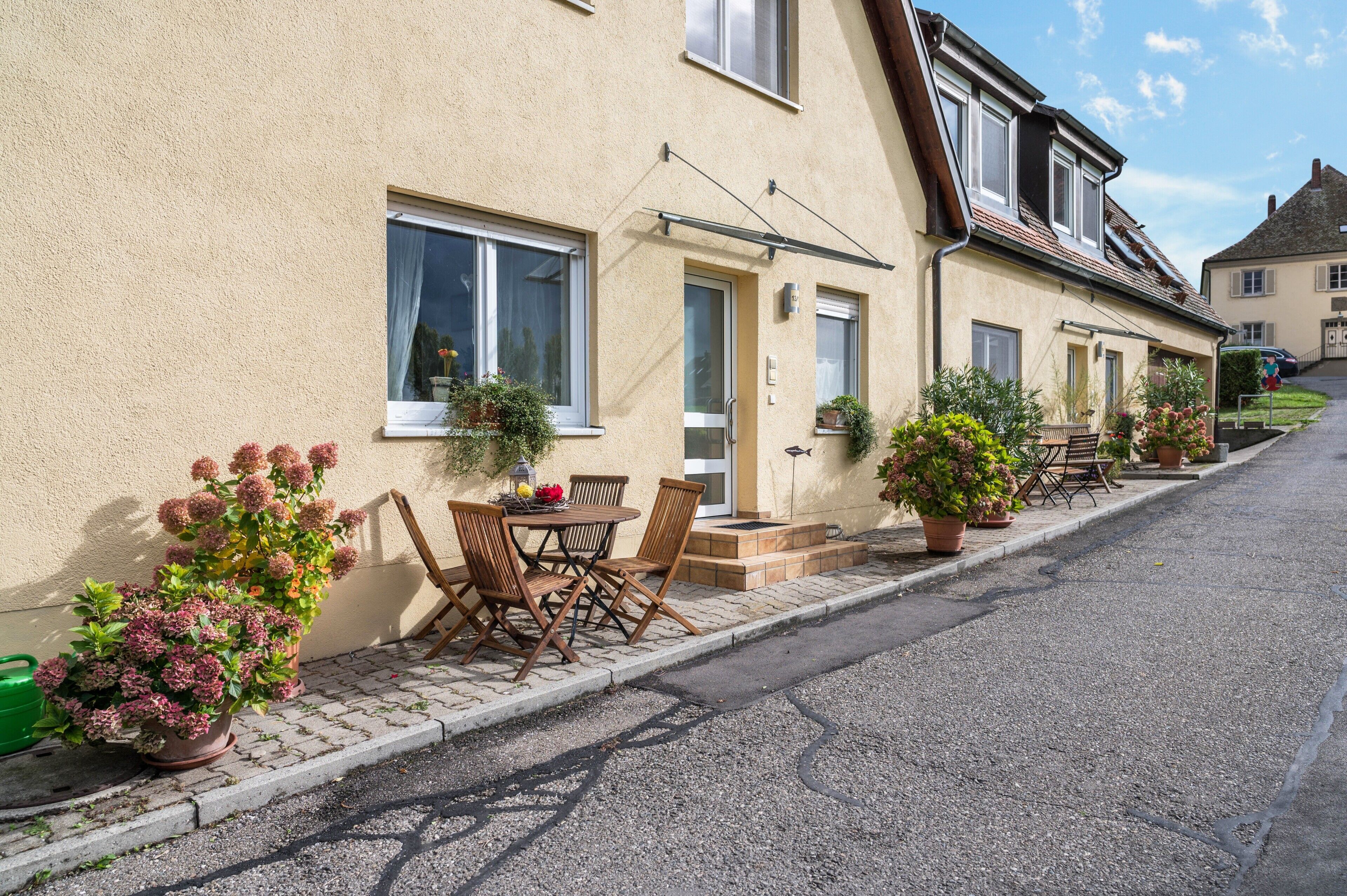Une rangée de maisons bordant une rue pavée, avec des places assises à l’extérieur et des plantes en pot.