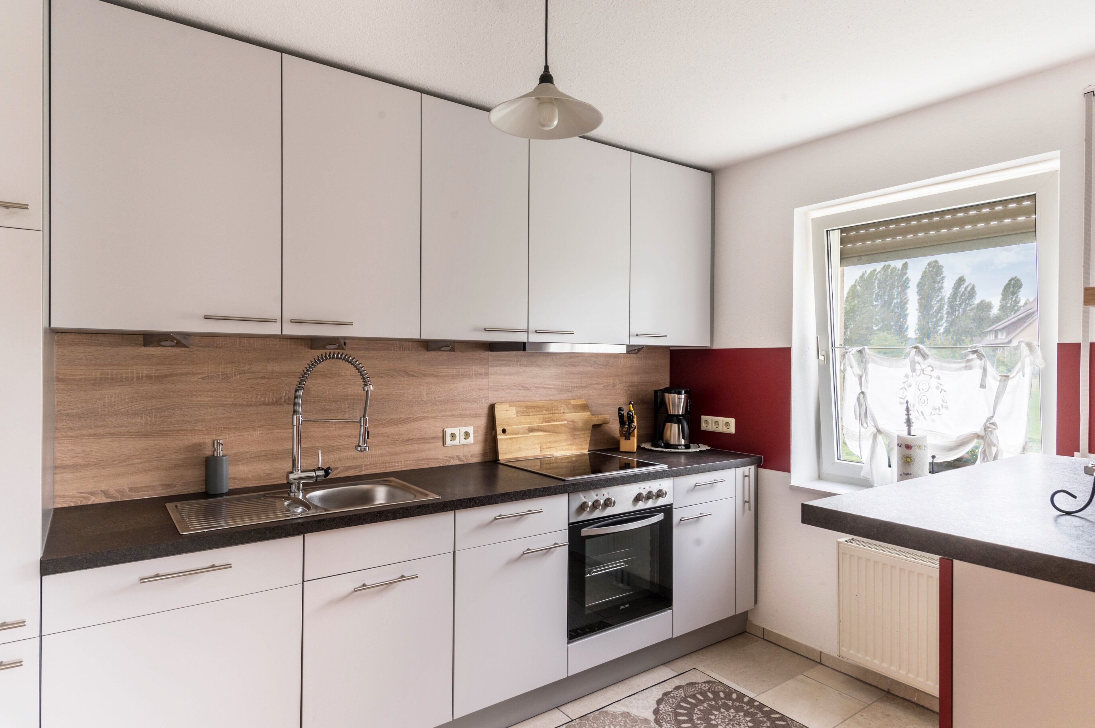 Eine moderne Küche mit weißen Schränken, einem schwarzen Backofen, einer Spüle und einem Fenster mit Jalousien.