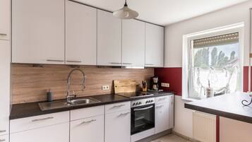 Eine moderne Küche mit weißen Schränken, einem schwarzen Backofen, einer Spüle und einem Fenster mit Jalousien.